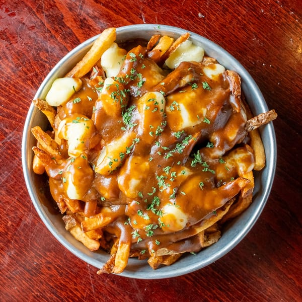 A metal bowl filled with golden french fries, cheese curds, and rich brown gravy, garnished with parsley.