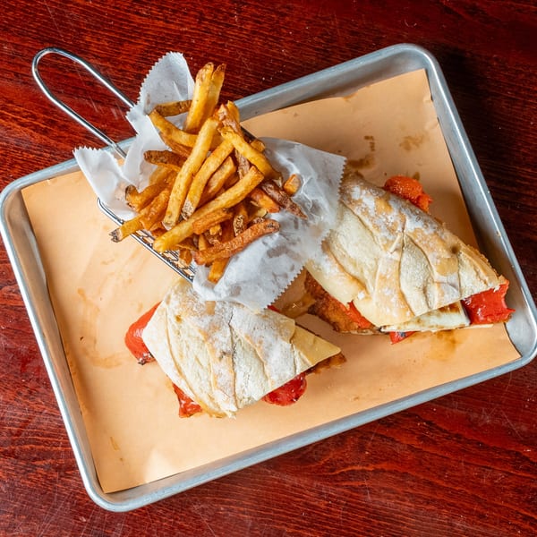 Two sandwiches with red peppers and cheese, served with a side of fries in a metal basket.