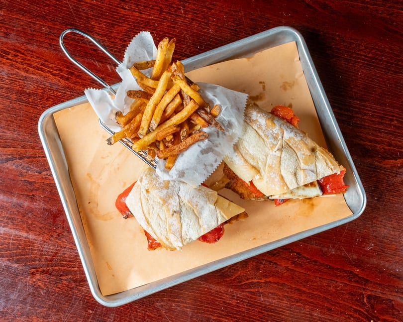 Two sandwiches with red peppers and cheese, served with a side of fries in a metal basket.