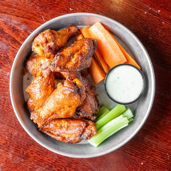 A metal tray of crispy chicken wings with carrot sticks, celery, and a side of ranch dressing.