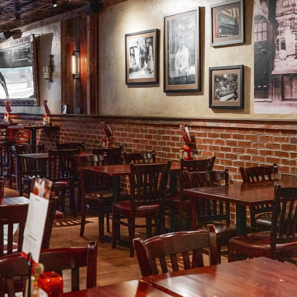 Interior of a restaurant with dark wooden tables and chairs, brick walls, and framed pictures.