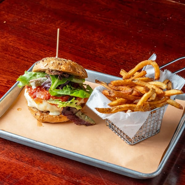 A burger with lettuce, tomato, and cheese, served with a side of fries on a metal tray.