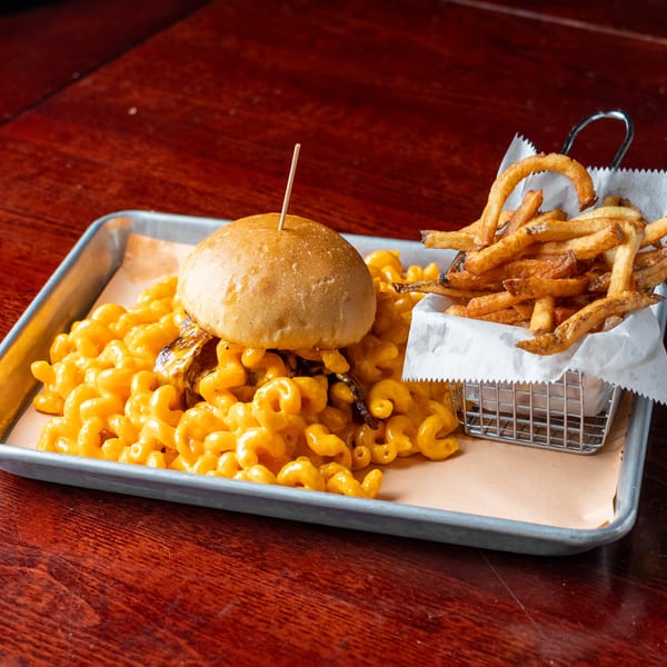 A mac and cheese burger with fries in a metal basket, served on a tray.