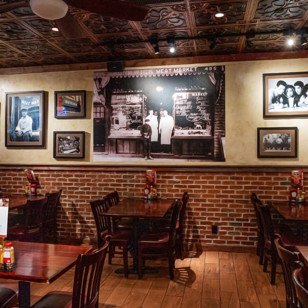 Restaurant interior with dark wooden tables and chairs, brick walls, and vintage framed photos.