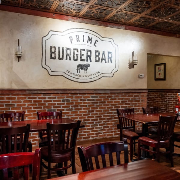 Interior of Prime Burger Bar with a large logo, brick walls, dark wooden tables, and chairs.